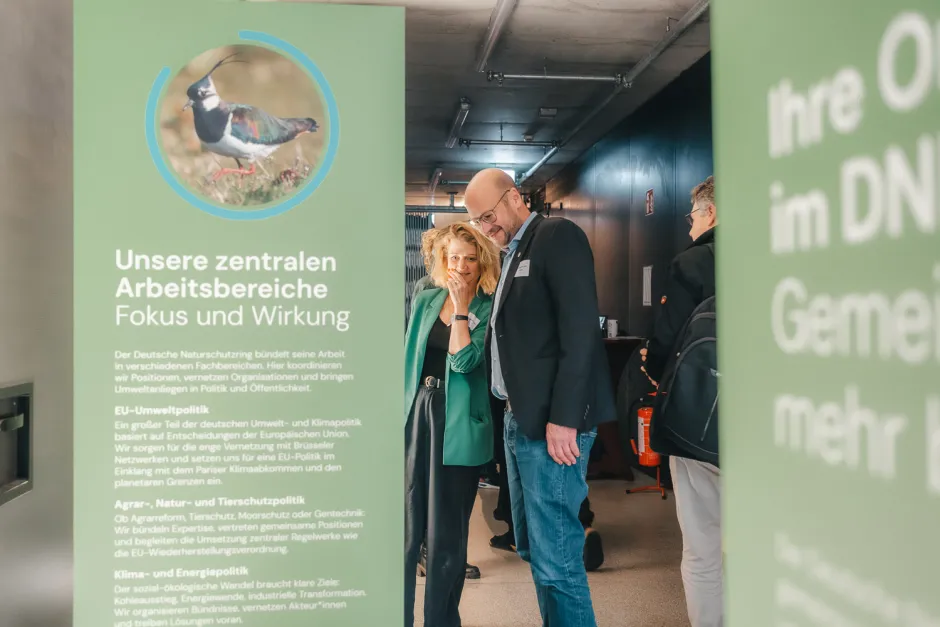 Blick durch die grünen Ausstellungstafeln auf zwei Besucher